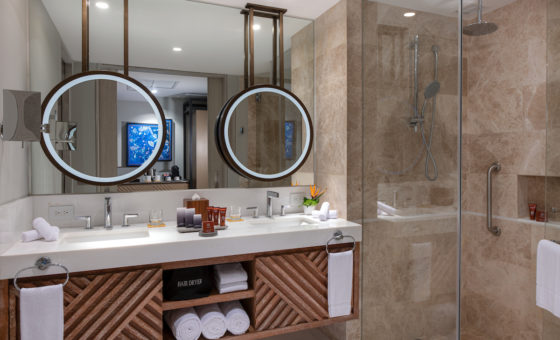 A hotel room bathroom with two circle mirror and essentials
